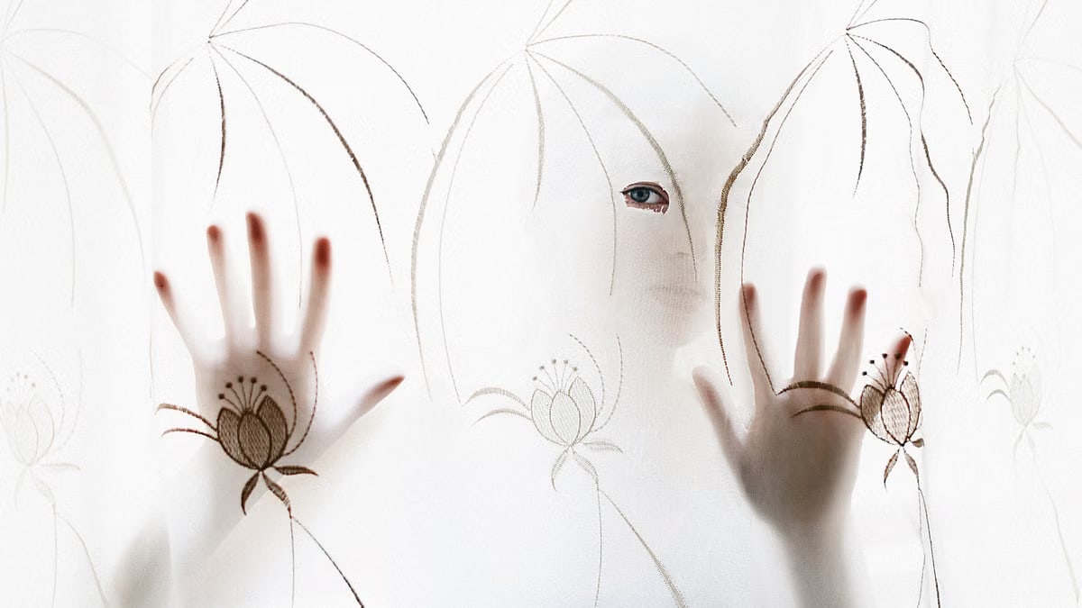 Artistic silhouette of a person with hands and eye visible through a decorative curtain.